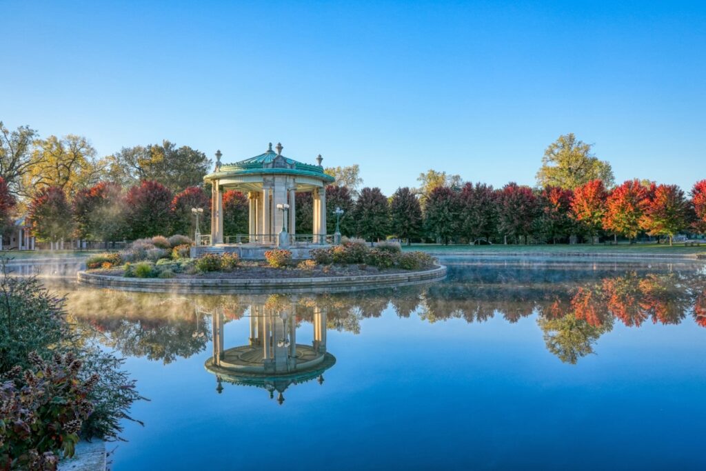 A gazebo in a park with trees and a pond