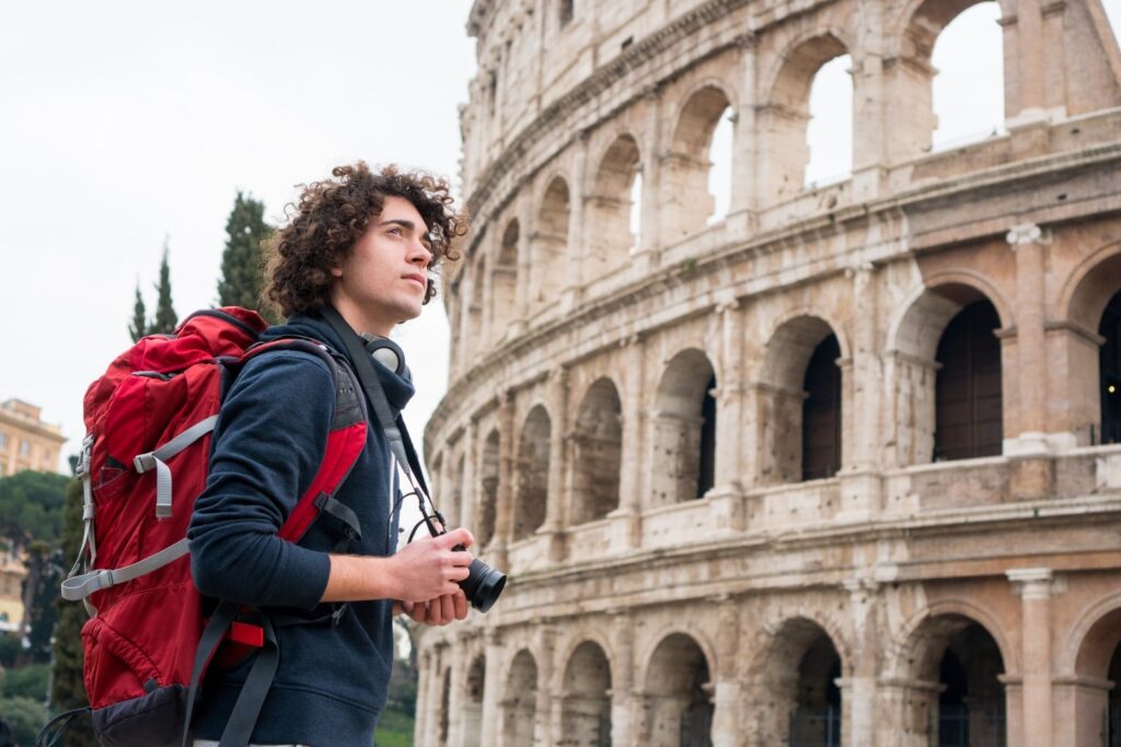 A person with a backpack and a camera in front of a large stone building